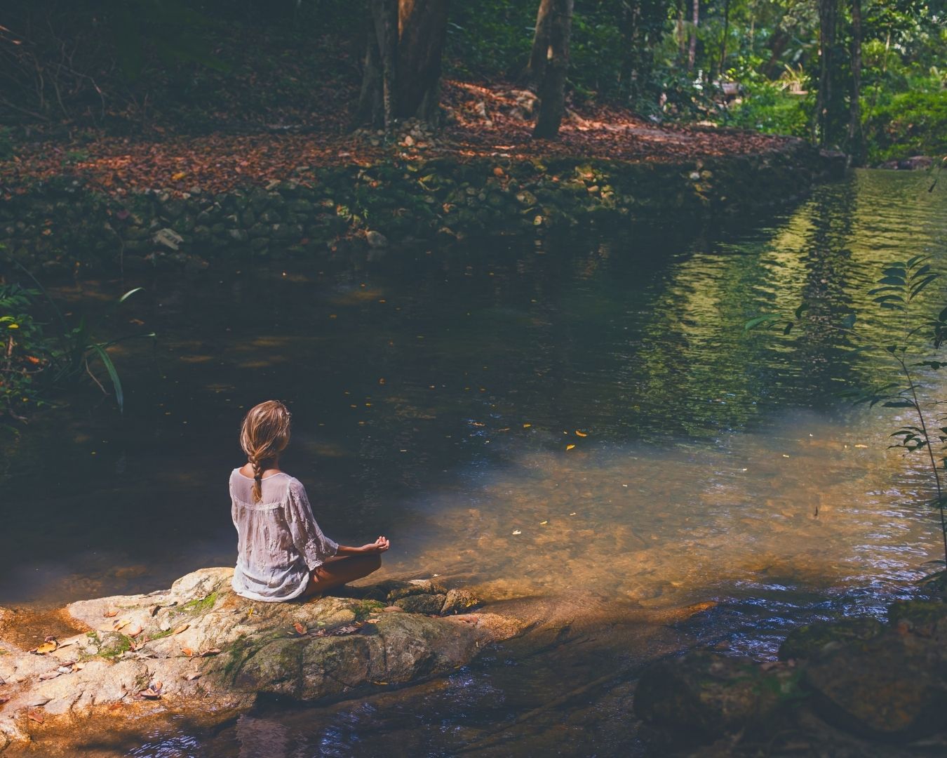 A woman practices meditation on a cliff edge, surrounded by majestic mountains and serene nature.